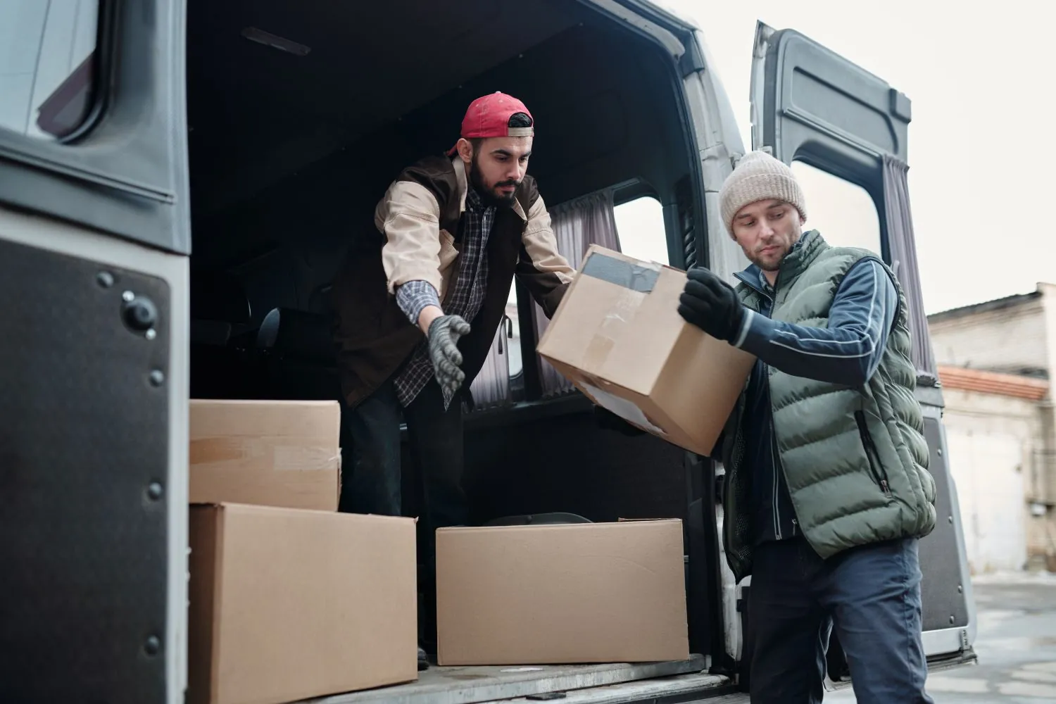 Two workers handling a cardboard box at the open back of a van